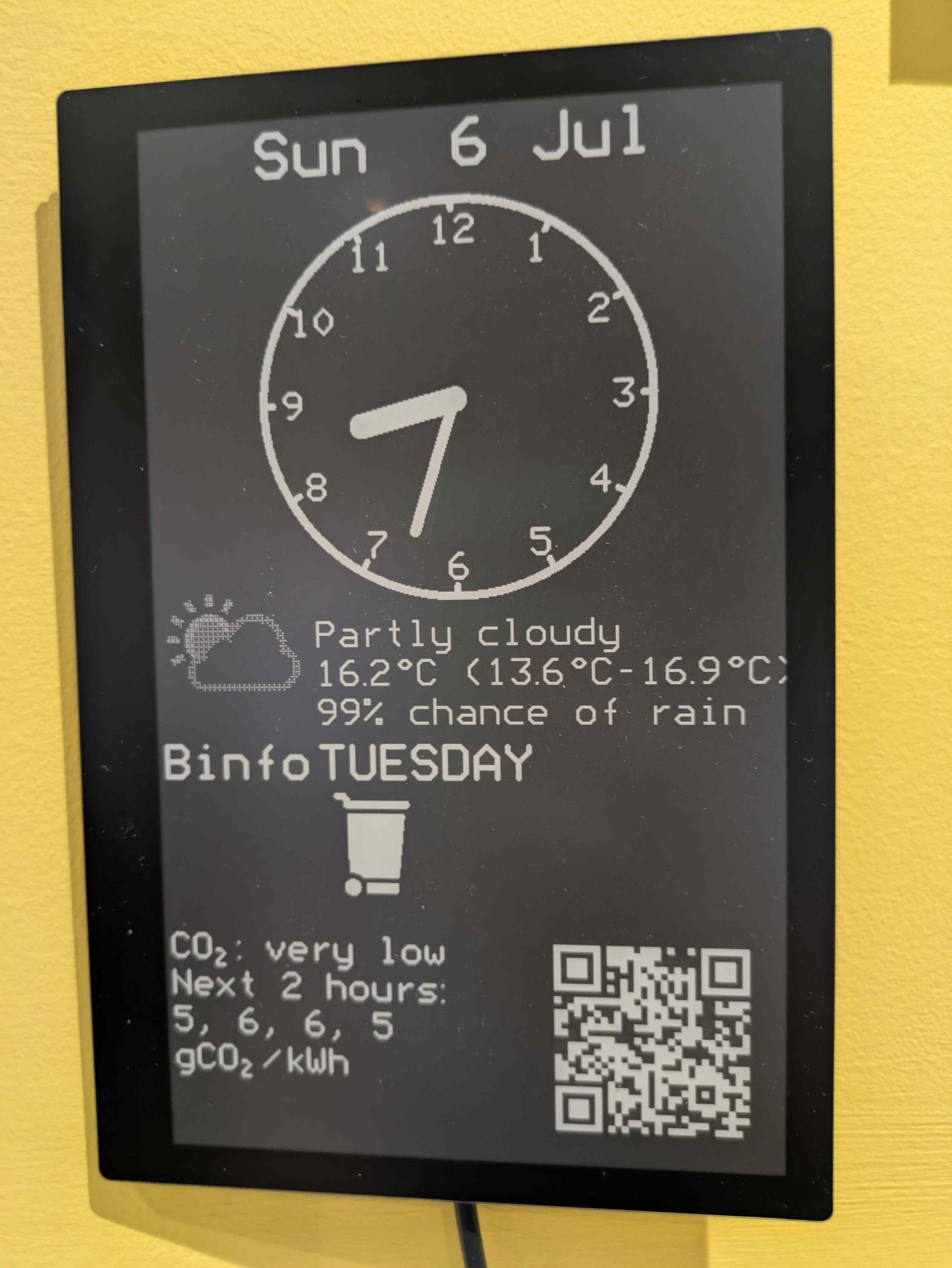A 7-inch e-paper display, showing the current date and time, a summarised weather forecast, the next bin collection day and type, the current grid carbon intensity and a QR code (with fake details) for my home WiFi network.